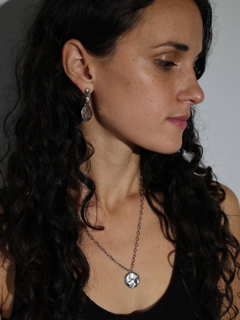 A model wearing the Consum Drop Earrings and Restituo Medallion Necklace in Recycled Sterling Silver by Bexon Jewelry 