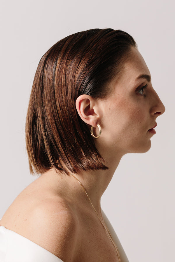A profile view of a model wearing Bexon Fine Jewelry Gloria Hoop Earrings in 14k recycled yellow gold with hinge and catch closure